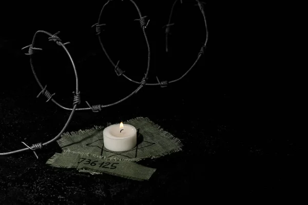 Burning candle, Jewish badge, prisoner number and barbed wire on black background with space for text. International Holocaust Remembrance Day