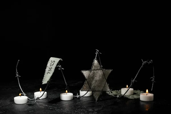 Prisoner number, Jewish badge, barbed wire and burning candles on black background with space for text. International Holocaust Remembrance Day