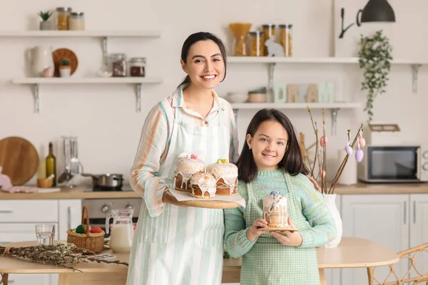 Little girl and her mother with prepared Easter cakes in kitchen