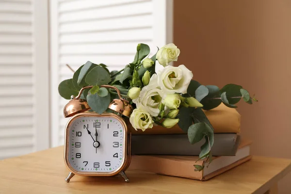 Bouquet of beautiful flowers, books and alarm clock on wooden table near color wall