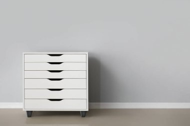 White chest of drawers near grey wall