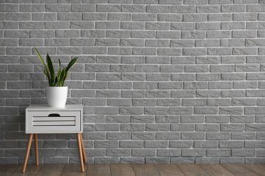 White table with drawer and houseplant near grey brick wall