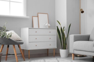 Chest of drawers with blank frames near light wall in living room