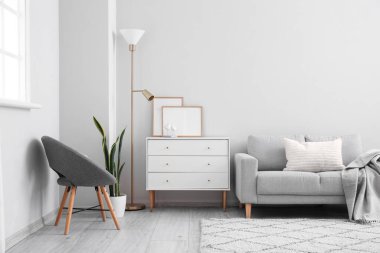 Interior of light living room with drawers, armchair and sofa