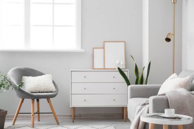 Interior of light living room with drawers, armchair and sofa
