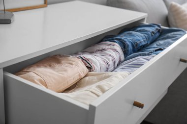 Open drawer with folded clothes in room, closeup