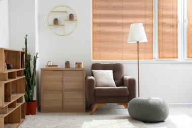 Interior of light living room with wooden drawers and armchair