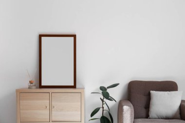 Interior of light living room with wooden drawers, blank frame and armchair