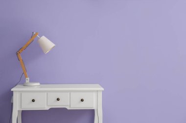 White table with drawers and lamp near lilac wall