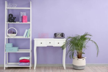 Interior of stylish room with table, shelving unit and houseplant