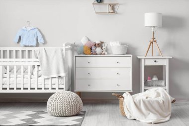 Interior of light children's bedroom with drawers, crib and table