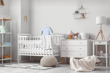 Interior of light children's bedroom with drawers, crib and table
