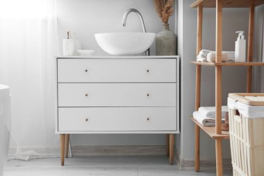 Chest of drawers with sink and vase in light bathroom