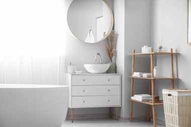 Interior of light bathroom with drawers, mirror and shelving unit