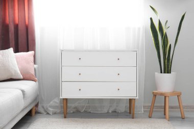 White chest of drawers and stool with houseplant in light living room