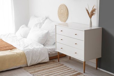 Interior of light bedroom with drawers and bed