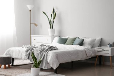 Interior of light bedroom with drawers, lamp and houseplants