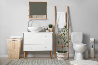 Interior of light bathroom with drawers, toilet bowl and laundry basket