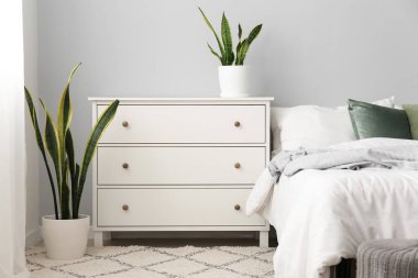 Interior of light bedroom with drawers and houseplants