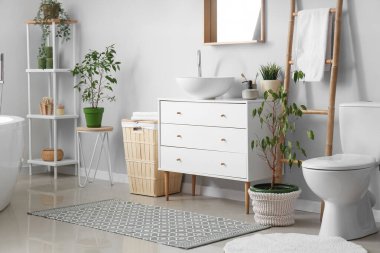 Interior of light bathroom with drawers, toilet bowl and laundry basket