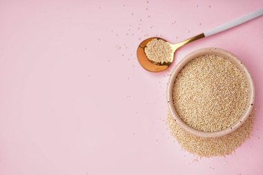 Bowl and spoon with amaranth seeds on pink background