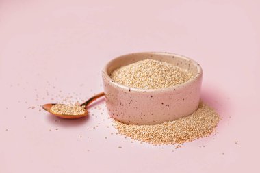 Bowl and spoon with amaranth seeds on pink background