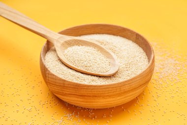 Wooden bowl of amaranth seeds on yellow background