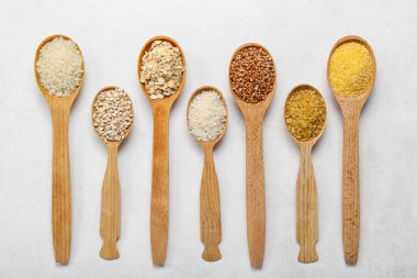 Wooden spoons of different cereals on light background