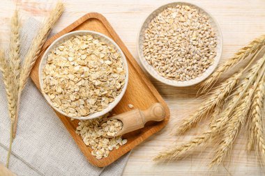 Bowls of raw oatmeal, pearl barley and spikelets on wooden background