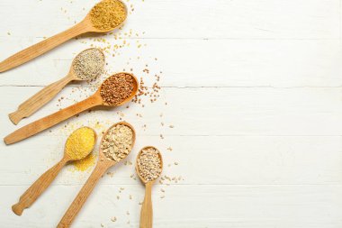 Spoons with different cereals on light wooden background