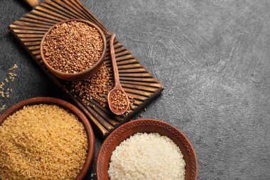 Bowls with buckwheat, rice and bulgur on dark background