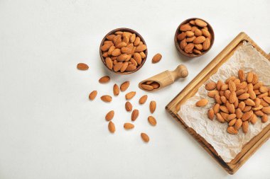 Wooden board and bowls with almond nuts on light background