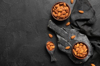 Composition with bowls of tasty almond nuts on dark background