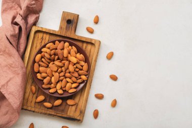 Wooden board with plate of almond nuts on light background