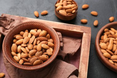 Wooden tray with plate of almond nuts on dark background, closeup
