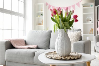 Vase with tulips on table in living room decorated for Easter celebration