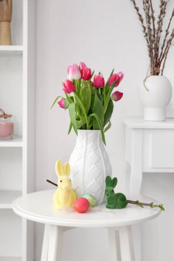 Vase with tulips, Easter eggs and rabbits on table in living room