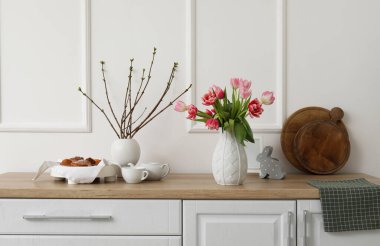 Vases with tulips, tree branches and Easter rabbit on counters in kitchen