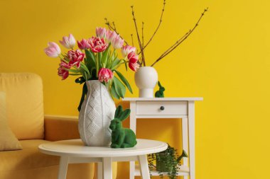 Vase with tulips and Easter rabbit on table in living room, closeup