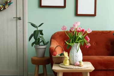 Vase with tulips, Easter bunny and eggs on end table in living room
