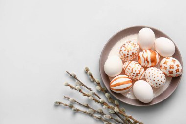 Plate with beautiful Easter eggs and willow branches on light background