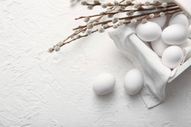 Basket with Easter eggs and willow branches on light background