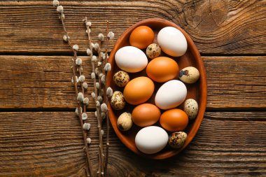 Plate with Easter eggs and willow branches on wooden background