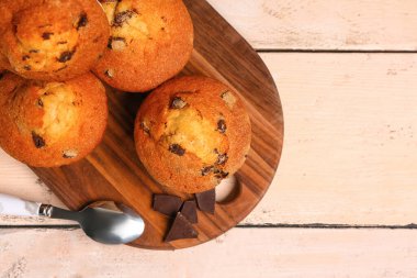 Board with delicious muffins and chocolate on white wooden background