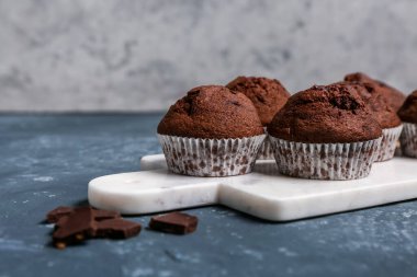 Board with delicious chocolate muffins on grey grunge background