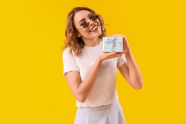 Happy young woman with gift on yellow background