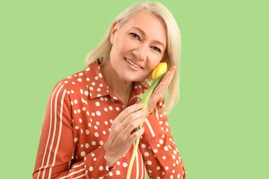 Beautiful mature woman with tulip on green background