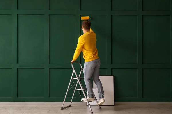 Young man with roller and ladder painting green wall