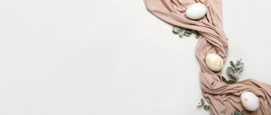 Beautiful Easter eggs, eucalyptus branches and cloth on light background with space for text