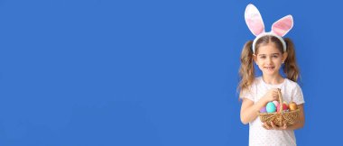 Little girl with Easter eggs and bunny ears on blue background with space for text